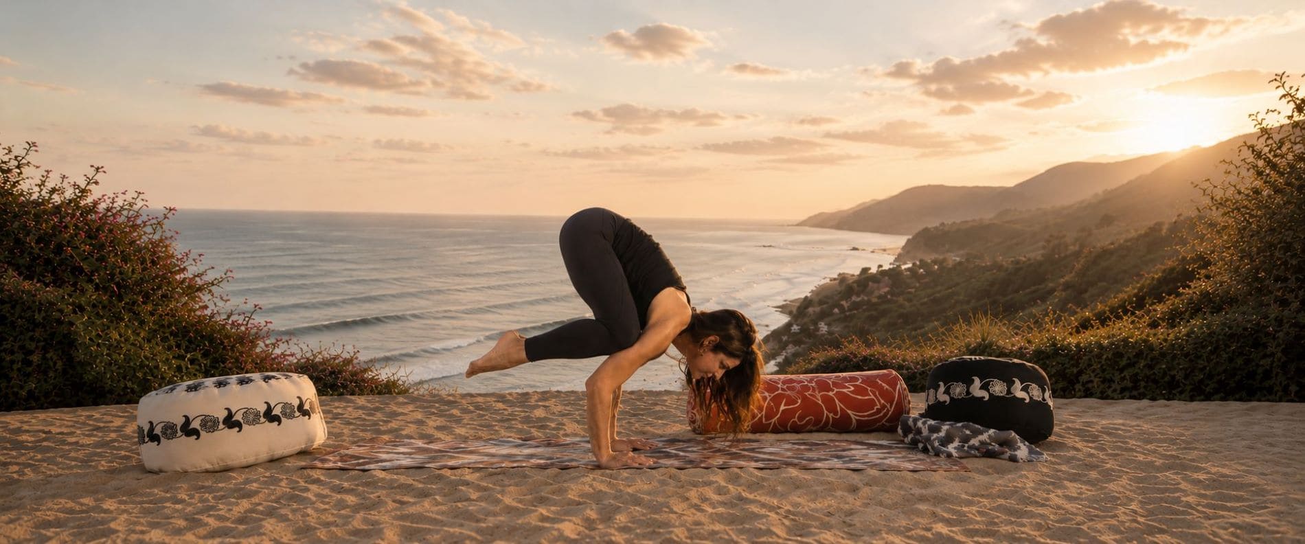 Mujer practicando yoga al atardecer frente al mar sobre una esterilla SunKiss, rodeada de bolsters y zafus artesanales en un entorno natural.